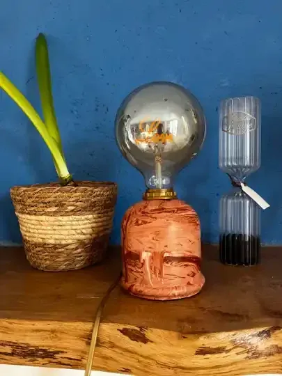 Lampe en résine minérale terracotta posée sur une étagère en bois avec plante