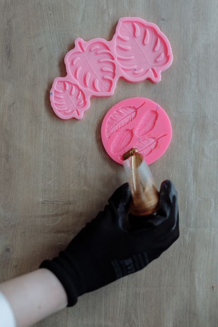 Main gantée coulant de la résine dans des moules en silicone en forme de feuilles